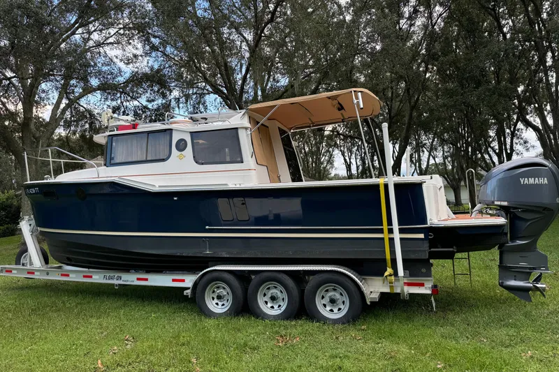Slide: The Image of 2024 Ranger Tugs R-27 boat on trailer with Yamaha outboard motor, parked on grass. - 99