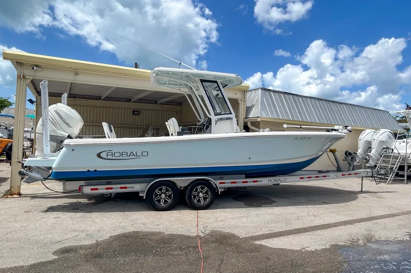 The Image of 2023 Robalo 266 Cayman boat on trailer, parked outdoors under blue sky. - 0