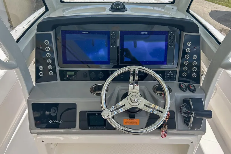 Slide: The Image of 2023 Robalo 266 Cayman helm with dual Simrad displays and chrome steering wheel. - 9