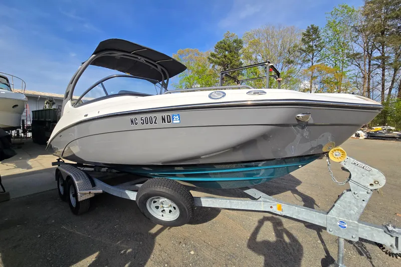 The Image of 2022 Yamaha Boats 212S on trailer, parked outdoors with trees in background. - 0