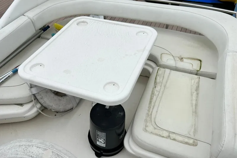 Slide: The Image of 1999 Sea Ray 400 Sedan Bridge interior with white seating and table, showing signs of wear. - 20