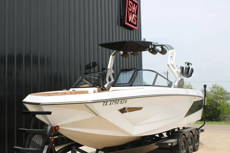 Slide: The Image of 2021 Nautique Super Air Nautique G25 boat on trailer, parked near a black building. - 3