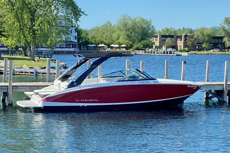 Slide: The Image of 2021 Regal LS6 boat docked on a serene lake with lush greenery. - 2