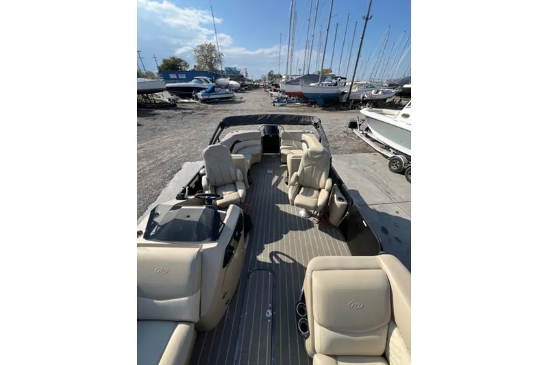 Slide: The Image of 2020 Manitou Oasis 250 pontoon boat interior with beige seating at a marina. - 10