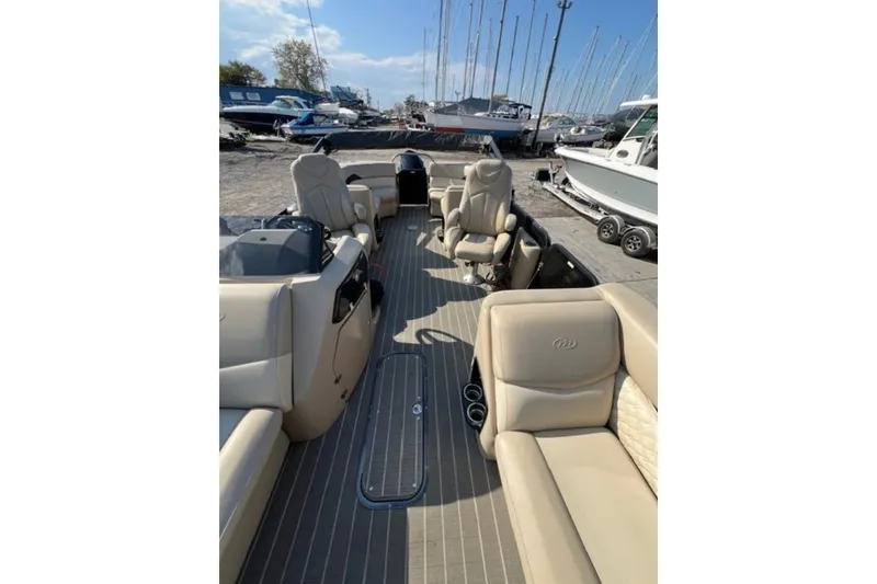 Slide: The Image of 2020 Manitou Oasis 250 pontoon boat interior with beige seating, docked near sailboats. - 7