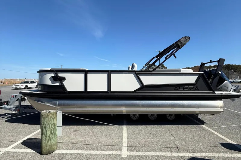 Slide: The Image of 2026 Alera M23Q pontoon boat parked in a lot under clear blue sky. - 5