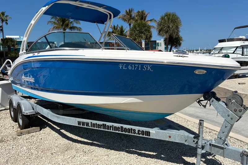 Slide: The Image of 2019 Chaparral 21 H2O Sport boat on trailer, blue and white, parked near marina. - 2