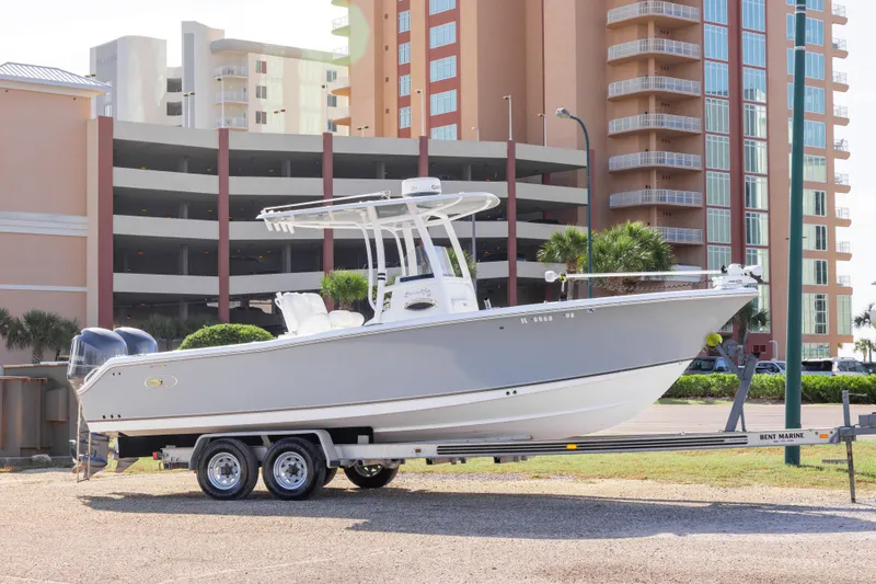 The Image of 2014 Sea Hunt Gamefish 25 boat on trailer, parked near modern buildings. - 1