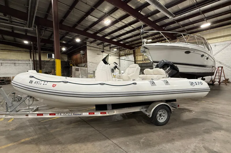 The Image of 2013 Mercury 560 inflatable boat on trailer in warehouse setting. - 0