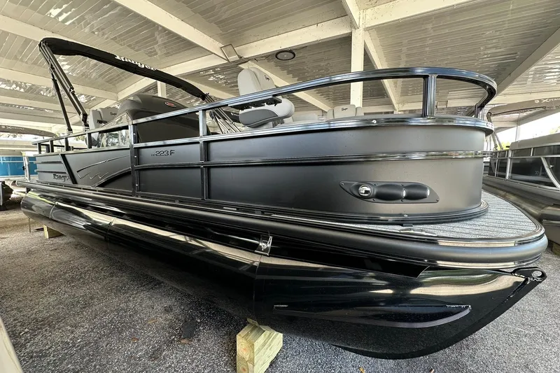 Slide: The Image of 2026 Ranger Reata 223FC pontoon boat in showroom, sleek black design under covered area. - 1