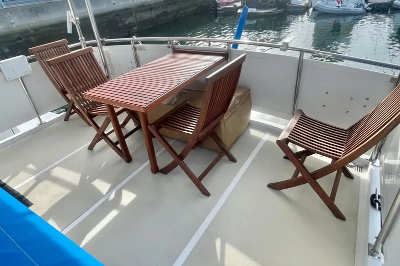 Slide: The Image of 1986 Tung Hwa aft cabin with wooden chairs and table on deck, docked by the water. - 8
