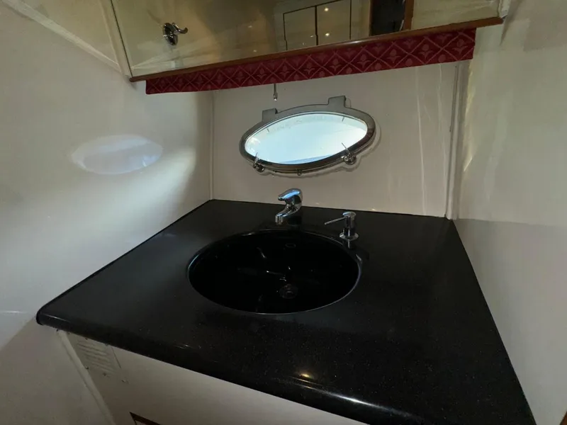 Slide: The Image of 2004 Ocean Alexander 42 yacht bathroom with black sink and oval porthole window. - 25