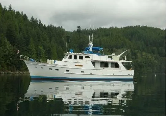 The Image of 1972 Grand Banks Alaskan 55 yacht on calm water, surrounded by lush green forest. - 0
