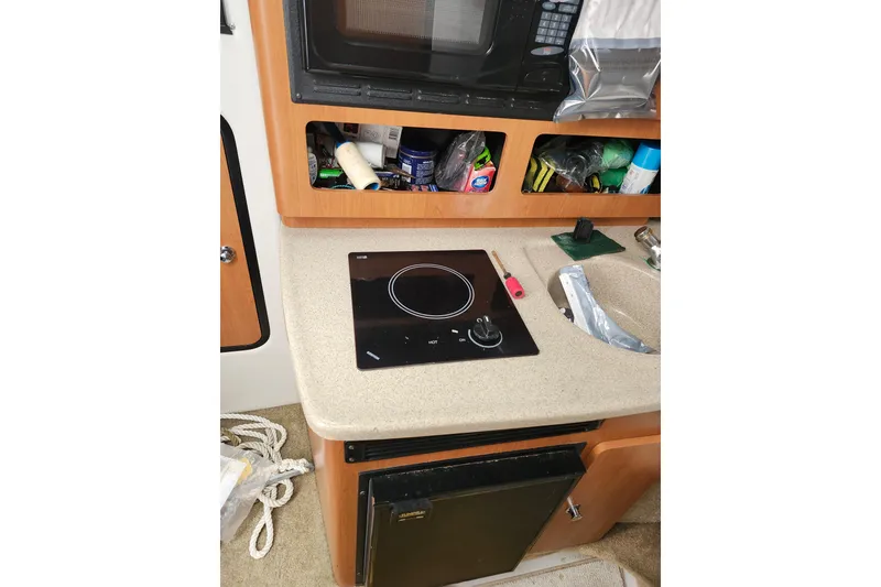 Slide: The Image of 2005 Crownline 275 CCR boat interior with kitchenette, featuring stove, microwave, and storage. - 14