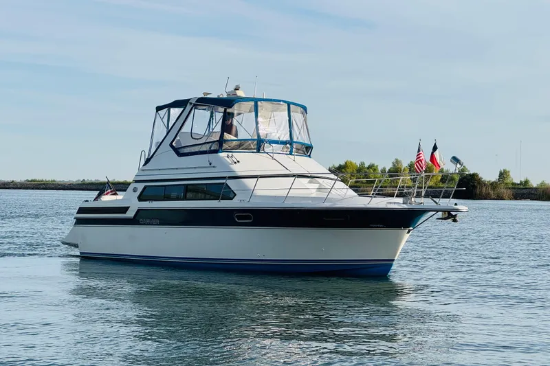 Slide: The Image of 1989 Carver 38 Santego yacht on calm water, featuring a sleek design and multiple flags. - 2