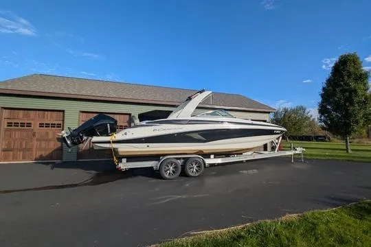Slide: The Image of 2023 Crownline Eclipse E285 XS boat on trailer, parked near a garage. - 1