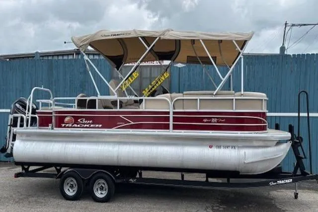 Slide: The Image of 2019 Sun Tracker SportFish 22 DLX pontoon boat on trailer, featuring a canopy and red accents. - 2