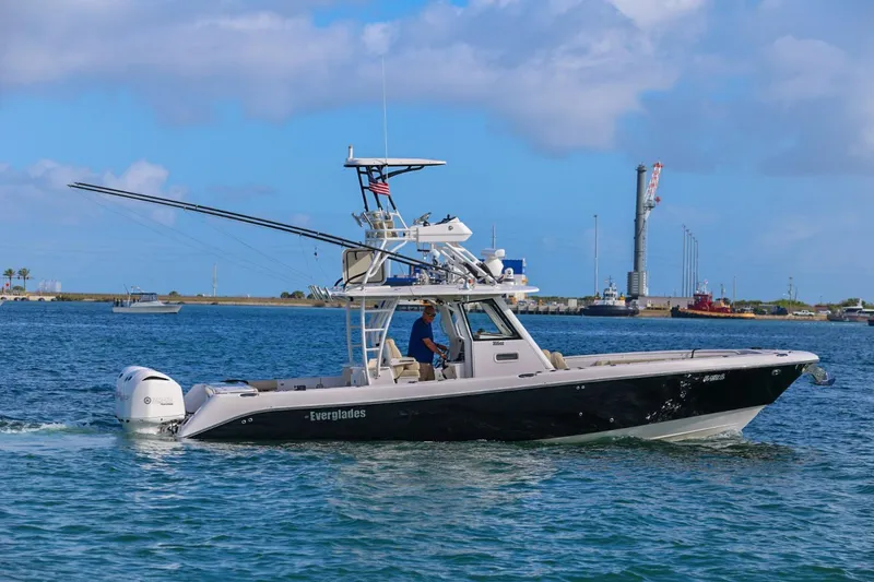Slide: The Image of 2017 Everglades 355 Center Console boat cruising on blue water near a harbor. - 20