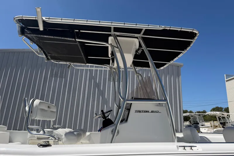 Slide: The Image of 2017 Sea Hunt Triton 210 boat with T-top, parked outdoors under clear blue sky. - 11