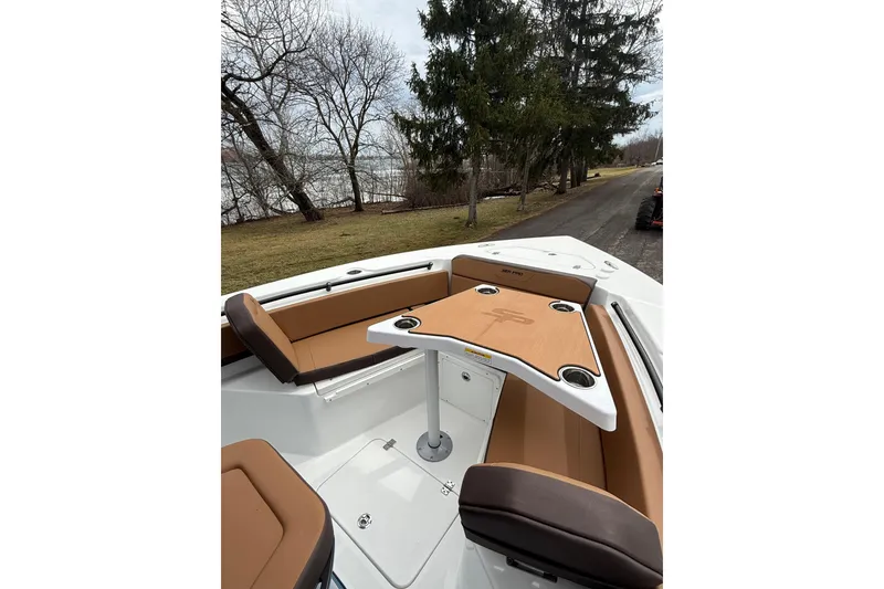 Slide: The Image of 2026 Sea Pro 245FLXR Sandbar boat interior with tan seating and table, near a lakeside path. - 14