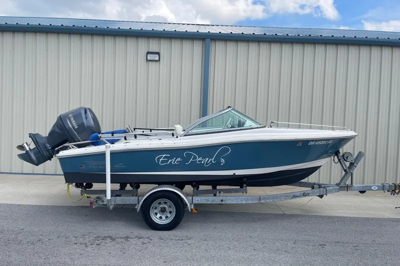 The Image of 2013 Pioneer 175 Venture boat on trailer, blue and white, parked by a metal building. - 0