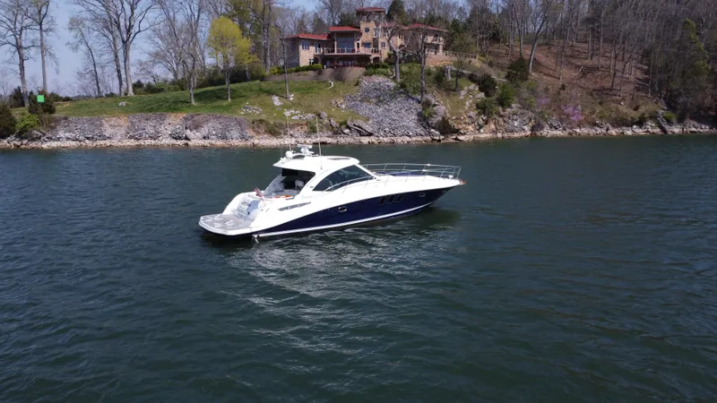 Slide: The Image of 2006 Sea Ray 48 Sundancer yacht cruising on a serene lake near a wooded shoreline. - 1