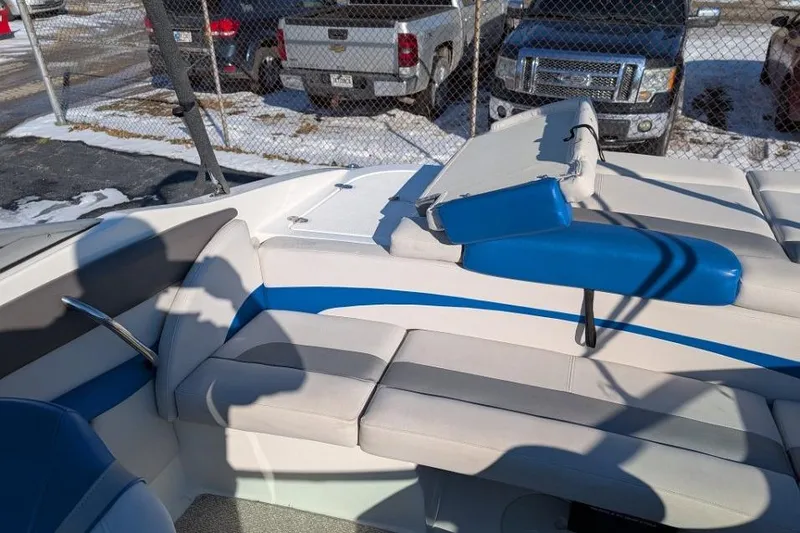 Slide: The Image of 2012 Rinker 216 Captiva Bowrider interior with blue and gray seating, parked near trucks. - 8