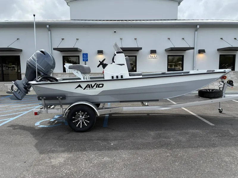 The Image of 2026 Avid 18CC ROGUE boat on trailer in front of building. - 1