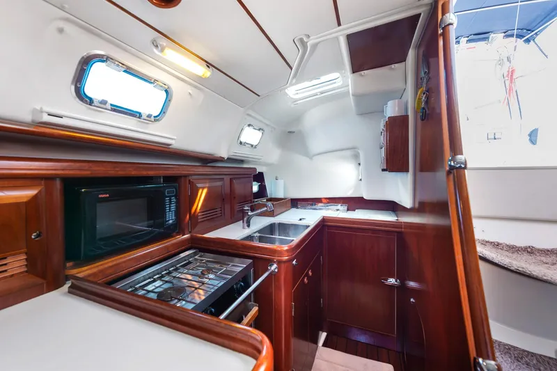 Slide: The Image of Interior of 2003 Beneteau 411 yacht, featuring kitchen and seating area with wood finish. - 5
