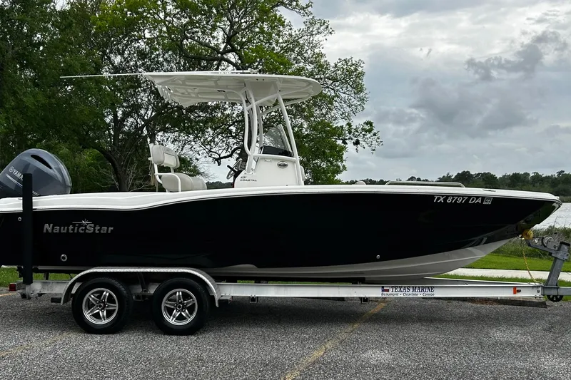 The Image of 2015 NauticStar 231 Coastal boat on trailer, parked outdoors with trees in background. - 0