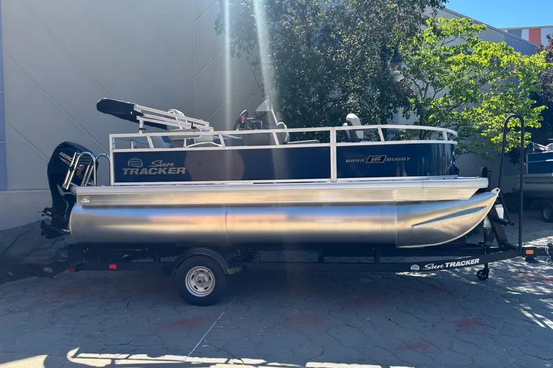 The Image of 2026 Sun Tracker Bass Buggy 16 XL Select pontoon boat on trailer, parked outdoors. - 0