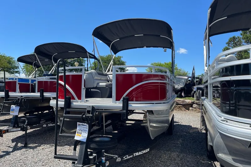 Slide: The Image of 2026 Sun Tracker Fishin' Barge 22 DLX pontoon boats displayed outdoors under blue sky. - 1