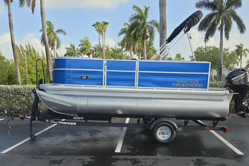 The Image of 2026 Sun Tracker Party Barge 16 DLX pontoon boat on trailer, parked with palm trees in background. - 0