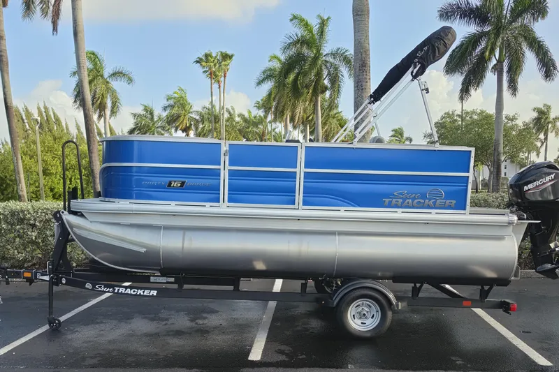 Slide: The Image of 2026 Sun Tracker Party Barge 16 DLX pontoon boat on trailer, parked with palm trees. - 67
