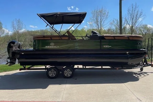 The Image of 2026 Regency 230 DL pontoon boat on trailer, green and black design, parked outdoors. - 0