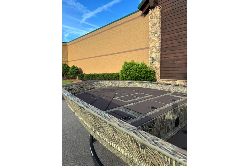 Slide: The Image of 2026 Tracker Grizzly 2072 CC boat with camouflage design, parked outdoors near a building. - 2