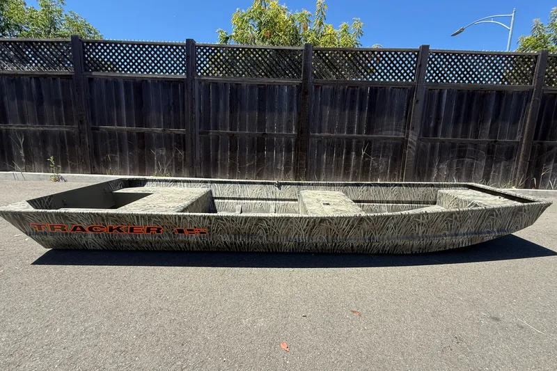 The Image of 2026 Tracker Grizzly 15 Jon boat on pavement, wooden fence background. - 0