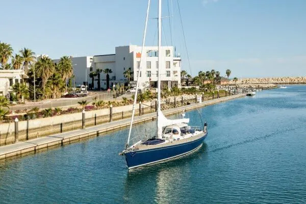 Slide: The Image of Sailboat "Gorbon Custom 66" (1997) cruising in a scenic marina with palm trees and buildings. - 245