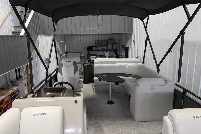 Slide: The Image of 2018 Lund LX220 Pontoon interior with plush seating and canopy in a storage facility. - 11
