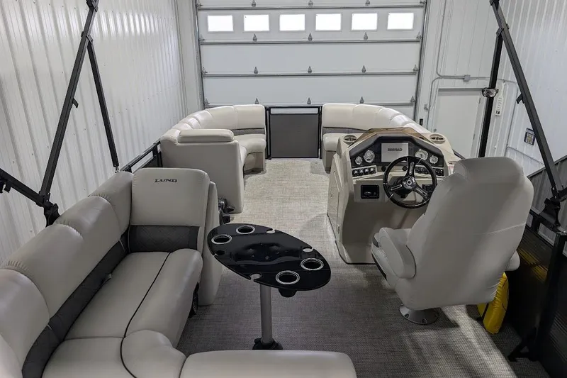 Slide: The Image of 2018 Lund LX220 Pontoon interior with plush seating and modern helm in a garage. - 23
