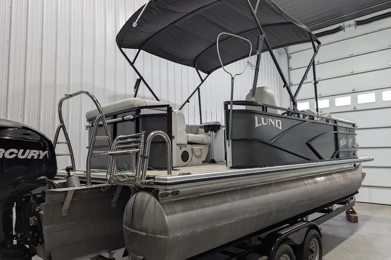 Slide: The Image of 2018 Lund LX220 Pontoon boat in a garage, featuring a Mercury outboard motor. - 3