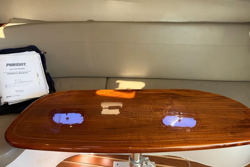 Slide: The Image of Interior of a 2005 Pursuit 3370 Offshore boat with a polished wooden table and owner's manual. - 19