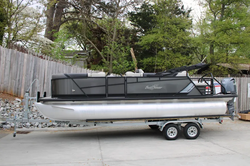 Slide: The Image of 2023 SunChaser Geneva Sport 23 SB pontoon boat on trailer, parked outdoors. - 0