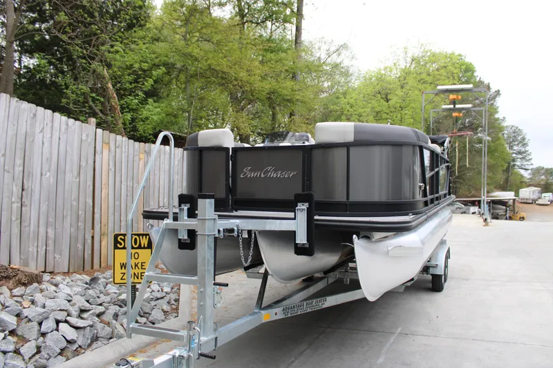 Slide: The Image of 2023 SunChaser Geneva Sport 23 SB pontoon boat on trailer, parked near wooden fence. - 4