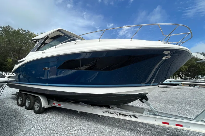 Slide: The Image of 2022 Sea Ray Sundancer 320 Outboard on trailer, sleek design, blue hull, parked outdoors. - 2