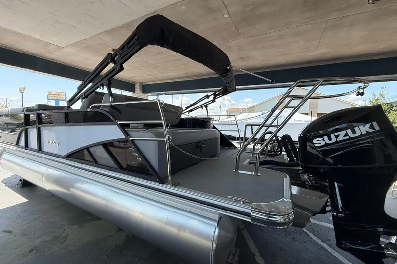 Slide: The Image of 2026 Crest Conquest 230 SLSC pontoon boat with Suzuki outboard motor, under a covered area. - 2