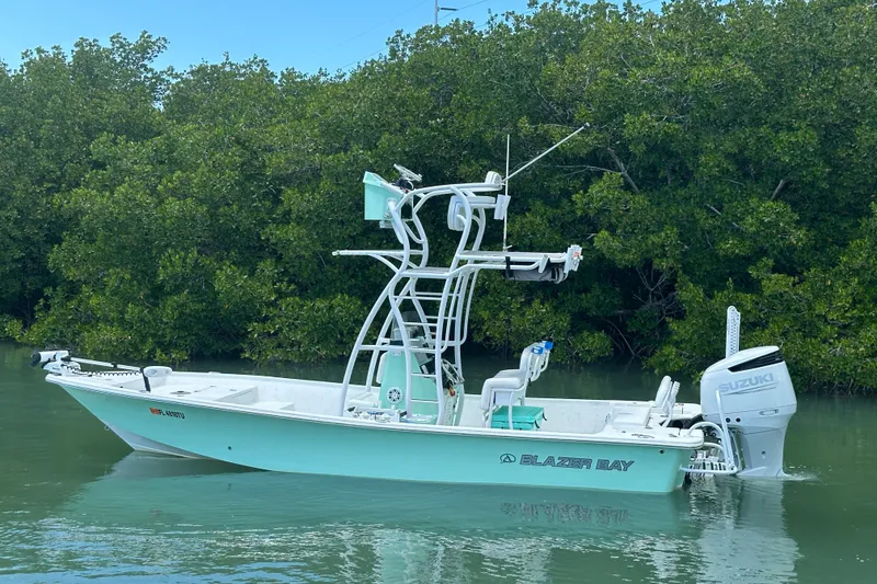 The Image of 2023 Blazer Bay 2400 boat with Suzuki engine, docked in calm waters near lush greenery. - 1