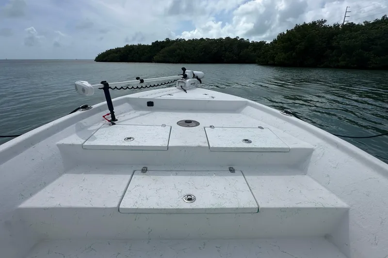 Slide: The Image of 2023 Blazer Bay 2400 boat deck on calm water, featuring storage compartments and trolling motor. - 17