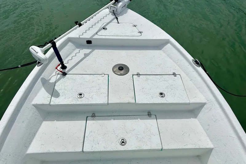 Slide: The Image of 2023 Blazer Bay 2400 boat deck with storage compartments and trolling motor on calm water. - 35