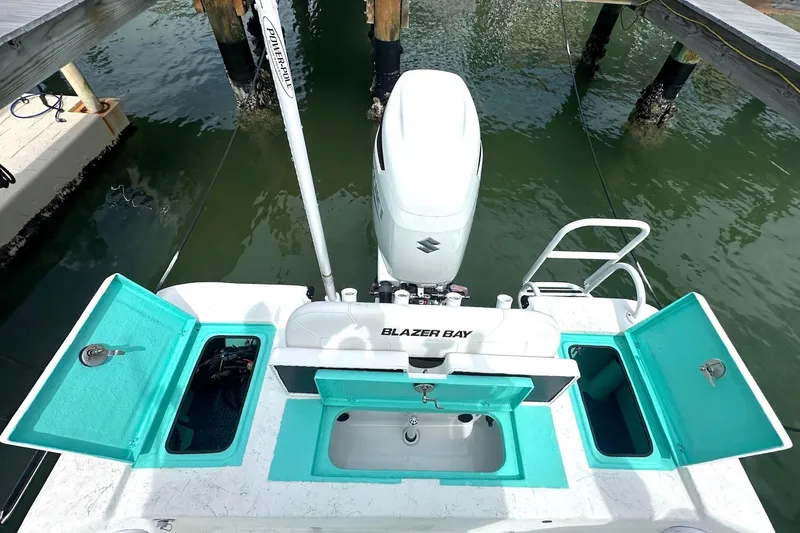 Slide: The Image of 2023 Blazer Bay 2400 boat with open storage compartments and motor, docked on water. - 38